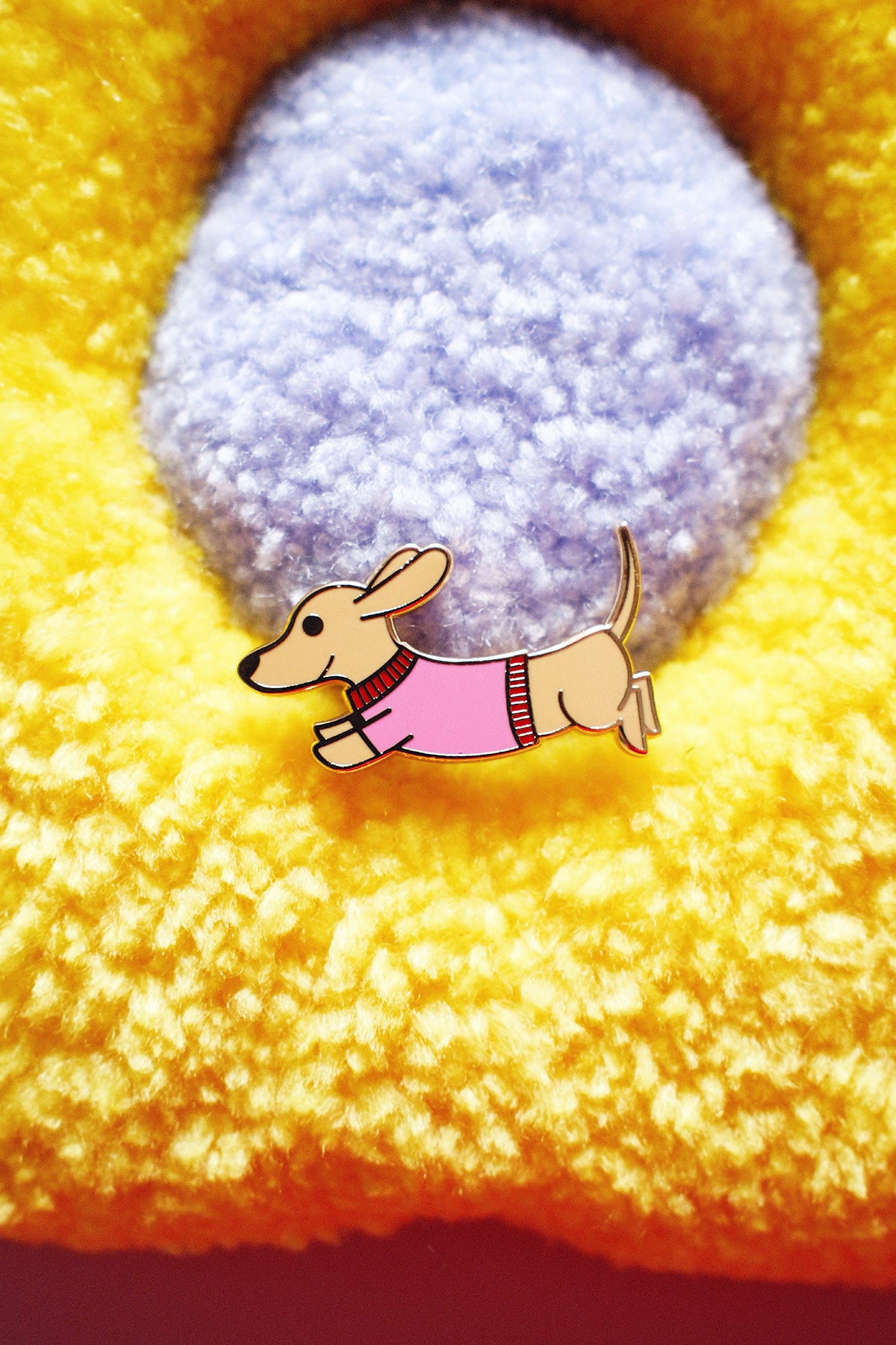 Pin's Teckel en métal avec motif de chien teckel, porté sur un fond neutre, illustrant un accessoire de mode original.